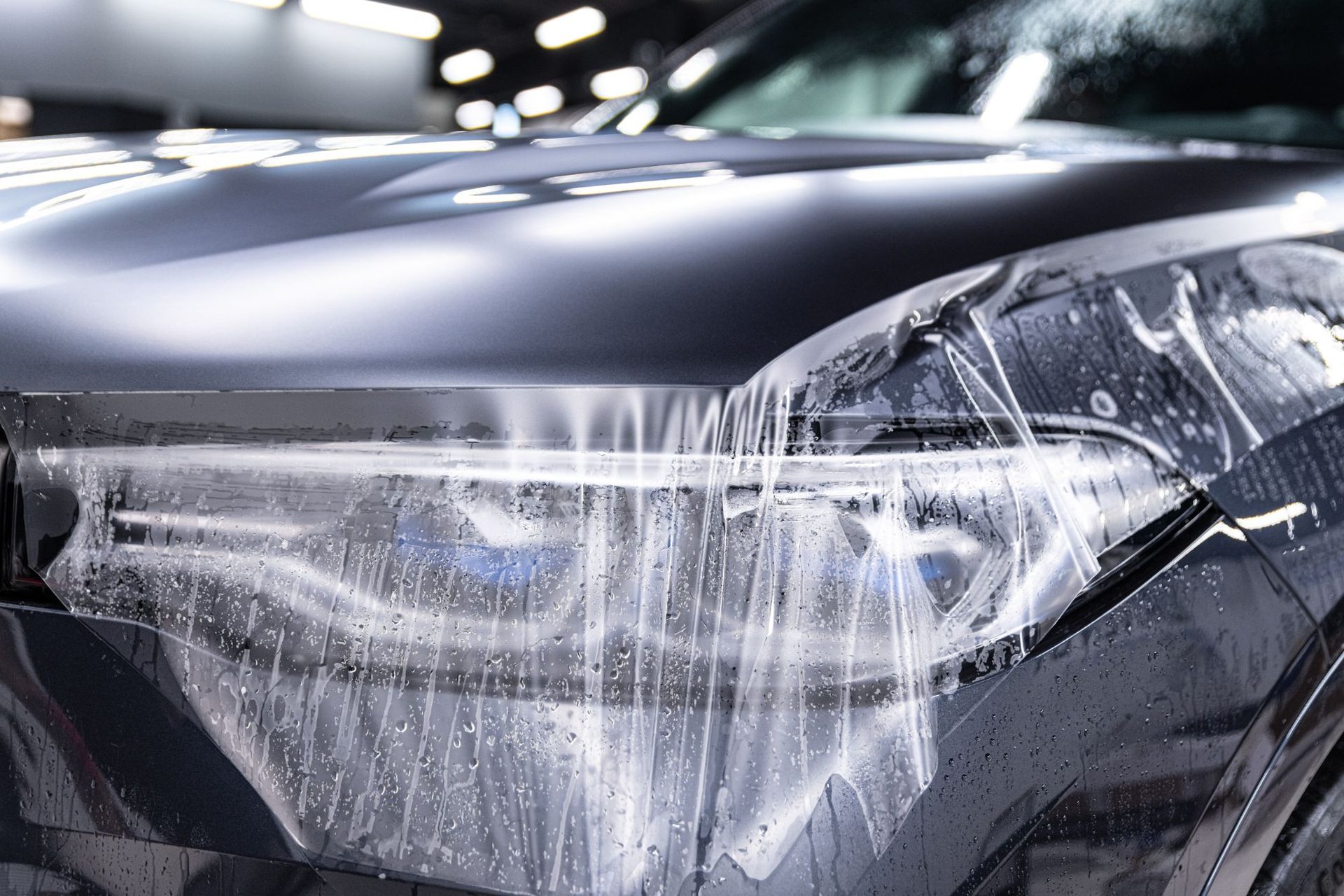 Transparente Lackschutzfolie wird über Scheinwerfer und Motorhaube eines dunklen Fahrzeugs gezogen